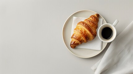 A minimalist flat lay featuring a cup of black coffee, a single croissant on a small plate, and a white napkin on a light grey background