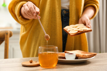 Woman pouring honey onto toast with banana at table indoors, closeup