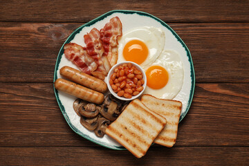 Plate with fried eggs, sausages, mushrooms, beans, bacon and toasts on wooden table, top view. Traditional English breakfast