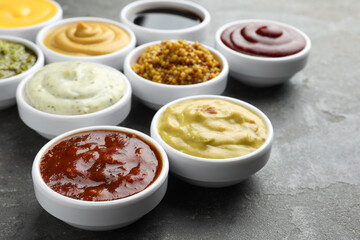 Many different sauces in bowls on grey table, closeup