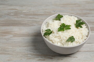 Tasty cooked rice with parsley in bowl on wooden table. Space for text