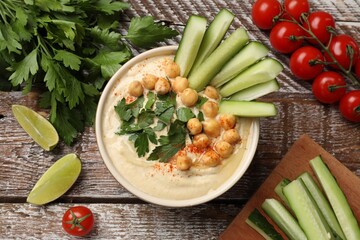 Tasty hummus with chickpeas in bowl and fresh products on wooden table, flat lay