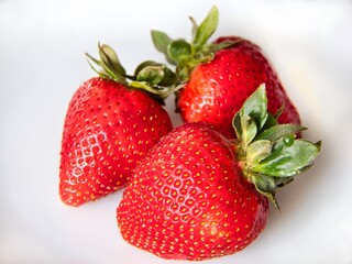 Close-up of three ripe, red strawberries with green leaves on white background