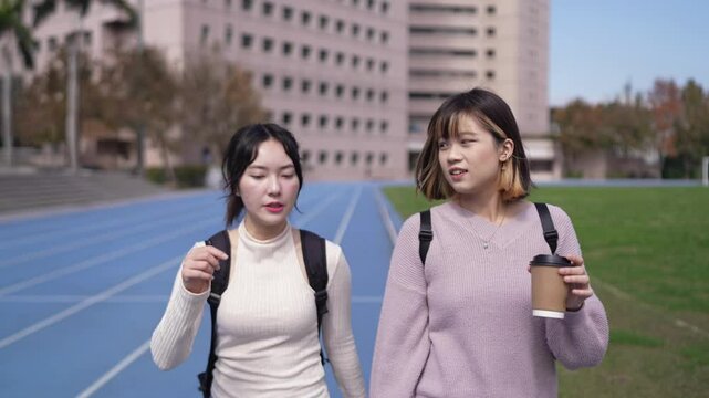 A slow-motion video of two young Taiwanese women in their early twenties walking together and chatting amicably on a university campus in Wenshan District, Taipei City, Taiwan.