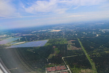 Aerial View of Expansive Solar Farm Amidst Verdant Forest and Urban Outskirts Under Clear Blue Sky