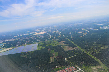 Aerial View of Expansive Solar Farm Amidst Verdant Forest and Urban Outskirts Under Clear Blue Sky