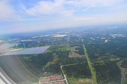 Aerial View of Expansive Solar Farm Amidst Verdant Forest and Urban Outskirts Under Clear Blue Sky