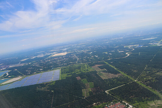 Aerial View of Expansive Solar Farm Amidst Verdant Forest and Urban Outskirts Under Clear Blue Sky