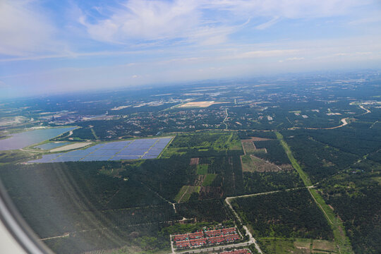 Aerial View of Expansive Solar Farm Amidst Verdant Forest and Urban Outskirts Under Clear Blue Sky
