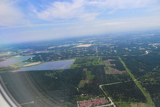 Aerial View of Expansive Solar Farm Amidst Verdant Forest and Urban Outskirts Under Clear Blue Sky