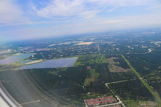 Aerial View of Expansive Solar Farm Amidst Verdant Forest and Urban Outskirts Under Clear Blue Sky