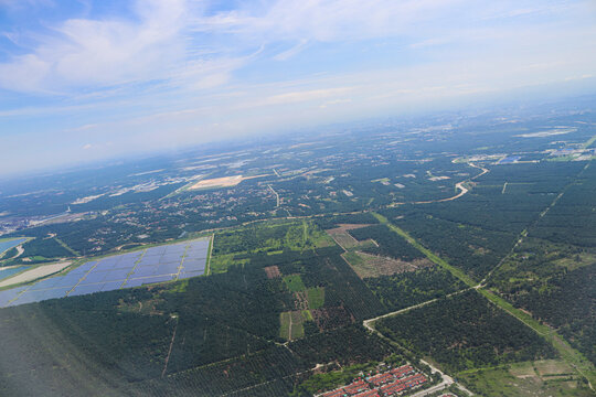 Aerial View of Expansive Solar Farm Amidst Verdant Forest and Urban Outskirts Under Clear Blue Sky