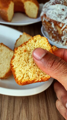 Hand holding a slice of cake and cornmeal cakes on the wooden table at background. Food from Minas Gerais state and from brazil.
