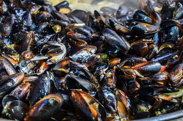 Freshly cooked mussels in their shells, glistening and piled together. Some shells are open, revealing the orange flesh inside. Ideal for culinary topics, seafood cuisine, and food industry content