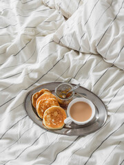 Breakfast in bed - pancakes, jam, a cup of tea on a metal tray on striped linen bed linen