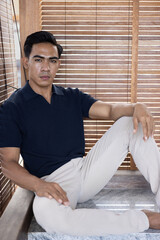 Handsome and good looking single gym fit and muscled male model with a black fashionable hairstyle and dark eyes, wearing a navy blue knitted polo and white pants while looking in the camera