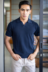 Handsome and good looking single gym fit and muscled male model with a black fashionable hairstyle and dark eyes, wearing a navy blue knitted polo and standing in the door opening