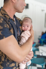 A thirty-something Indian Malaysian man holding a few-months-old baby at a stylish cafe in Selangor, Malaysia, on a sunny early summer afternoon.