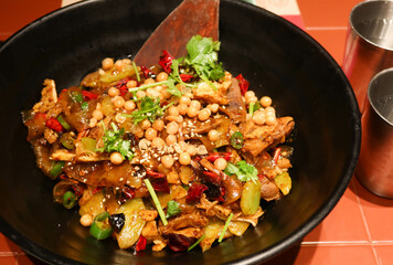 close up of Sichuan style spicy dry pot with peanut, beef tongue, beef stomach, celtuce, meat and noodles in a black bowl