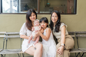 A twenty-something Malaysian woman holding a few-months-old baby, a six-year-old girl, and a twenty-something Chinese Malaysian woman spending time together at a stylish cafe in Selangor, Malaysia