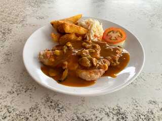 grilled golden bbq chicken chop pork cutlet meat with French fries wedges, coleslaw salad tomato and mushroom brown cream sauce in white plate on marble table western cafe halal food restaurant menu
