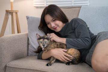 A woman lying on a couch, lovingly cuddling with her tortoiseshell cat. The intimate moment reflects the strong bond and comfort