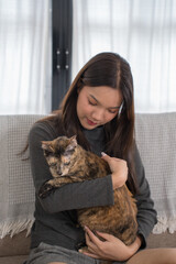  woman kneeling beside a couch, playfully interacting with her tortoiseshell cat sitting on the couch. The living room setting is warm