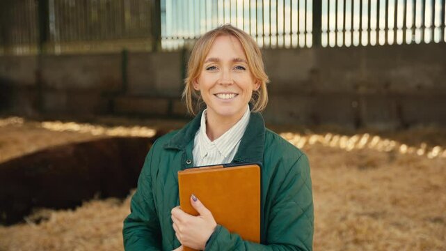 Portrait of smiling female farm worker or manager with digital tablet standing with cattle in barn - shot in slow motion