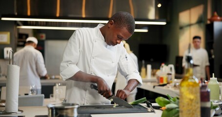Black man, chef and serious with cutting vegetables in kitchen at restaurant for fine dining, meal or creativity. Male employee, professional or cooker with food for culinary, hospitality or catering