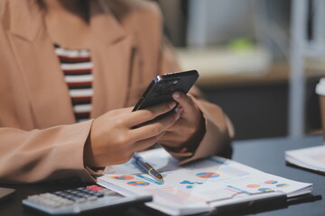 Young beautiful Asian businesswoman holding smartphone while working in the office room.
