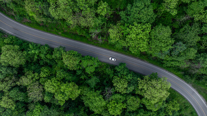 Aerial view electric vehicle car driving on asphalt road in mountain green forest, EV car electric vehicle car on forest road green energy and eco power, White electric car driving green forest road.
