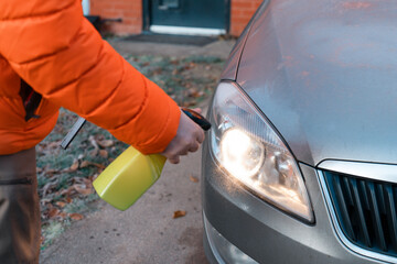 Person Cleaning Car Headlight With Spray Bottle in Front of Brick House