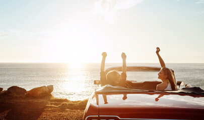 Friends, woman and freedom in car at beach with sunset, scenery and travel adventure with mockup space. Road trip, people and convertible vehicle on coast at ocean for sightseeing and sunrise view © ReeseArcurs/peopleimages.com