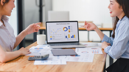Two businesspeople or an accountant team are analyzing data charts, graphs, and a dashboard on a laptop screen in order to prepare a statistical report and discuss financial data in an office.
