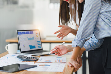 Two businesspeople or an accountant team are analyzing data charts, graphs, and a dashboard on a laptop screen in order to prepare a statistical report and discuss financial data in an office.