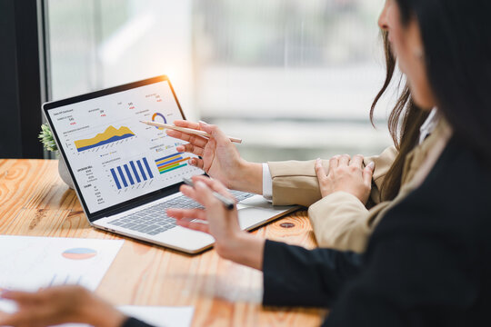 Two businesspeople or an accountant team are analyzing data charts, graphs, and a dashboard on a laptop screen in order to prepare a statistical report and discuss financial data in an office.