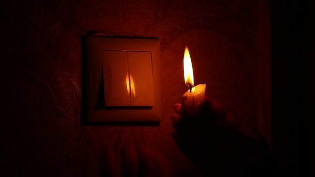 A woman's hand with a candle turns on and off the light switch in the dark, Ukraine without light, power outage