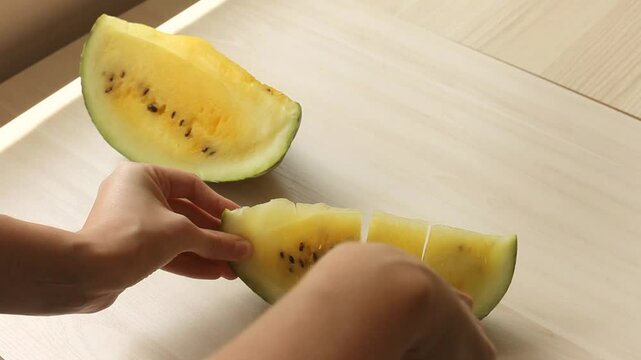 Hand cutting yellow watermelon on white wooden table