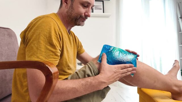 Man with painful knee and leg injury at home cooling down with ice pack.	
