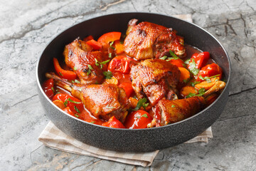 Homemade rooster stew with bell peppers, onions and carrots in a spicy tomato sauce close-up in a...