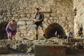 An archaeologist in a costume from the last century stands with a notepad against the backdrop of a...