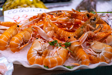 Assortment of fresh daily catch of prawns, seashells, molluscs on ice on fish market in Brittany, France, English translation: differens French names of seafood