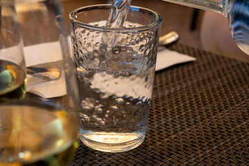 Waiter pouring mineral water from the glass bottle into a glass, food concept