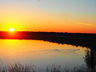 Sunset in hues of reddish-orange and yellow over the lake on a summer day.
