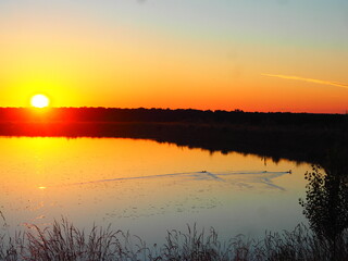 Obraz premium Sunset in hues of reddish-orange and yellow over the lake on a summer day.