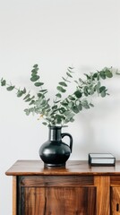 Fototapeta premium A simple, elegant arrangement of a eucalyptus plant in a black vase, placed on a wooden shelf against a white wall