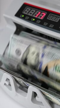Electronic money counting machine on the white table. UDS dollars calculated in the financial equipment. High angle view. Close up. Vertical video