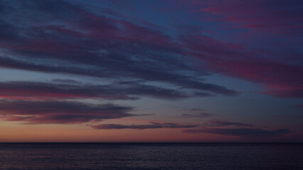 Beautiful sunset with purple clouds and flying birds over the sea