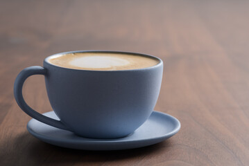 Fresh cappuccino in a blue cup on walnut table with copy space