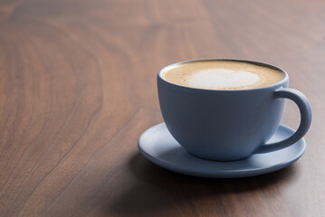 Fresh cappuccino in a blue cup on walnut table with copy space